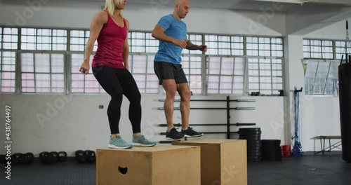 Fit caucasian woman and man jumping on pylo boxes at the gym photo