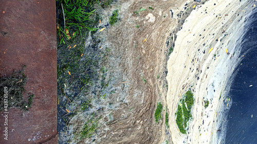 Polluted water with foam in a pond. Rusty pipe.