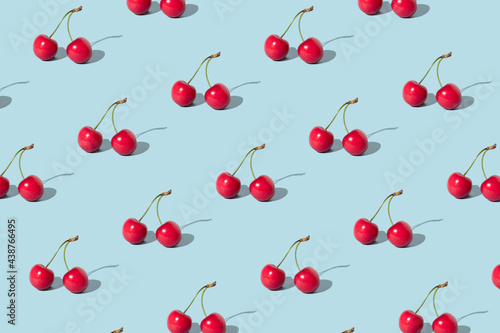Creative pattern made with red cherries on pastel blue background. Summer or spring fruit concept. Minimal aesthetic idea.