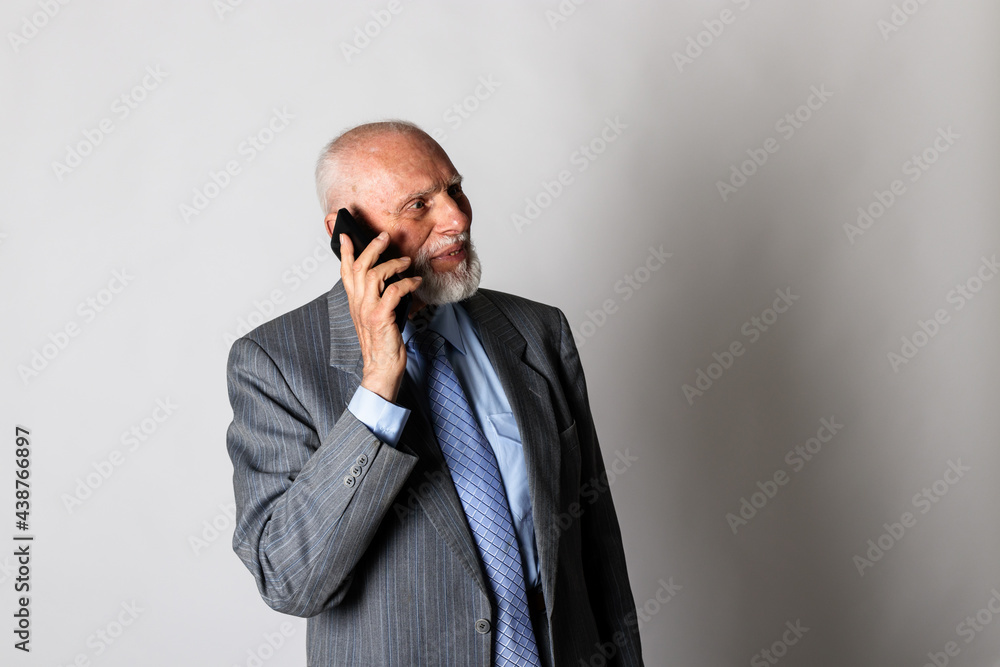 Old man in blue is using a smart phone on gray background with copy space. Old man in blue is using a smart phone on gray background with copy space.