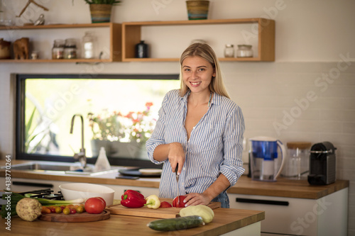 Happy woman preparing salad in the kitchen. Looking at camera.