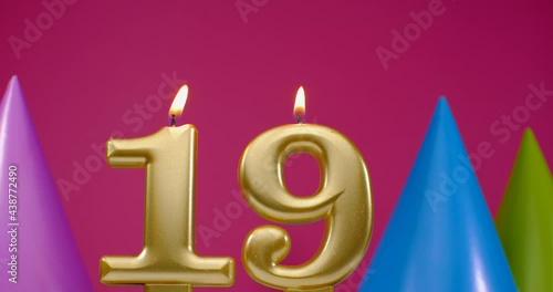 Burning birthday cake candle number 19. Happy Birthday background anniversary celebration concept. Birthday hat in the background photo