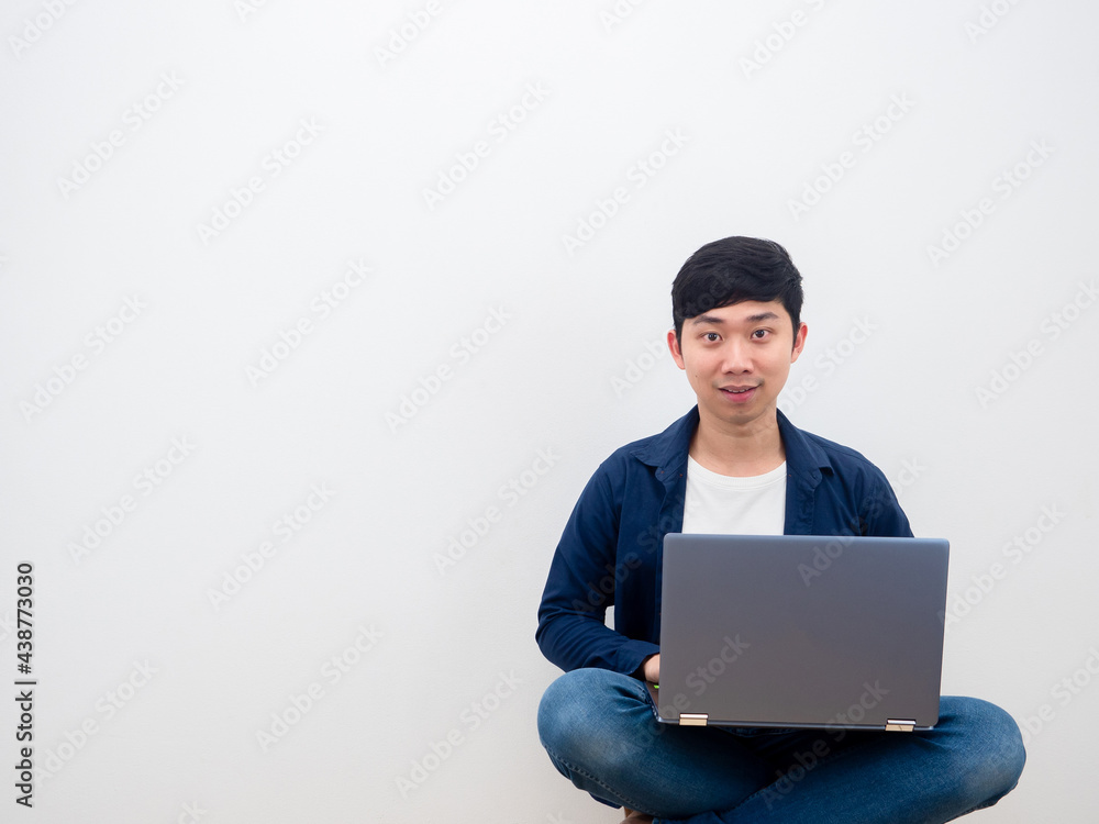 Asian man happy face using laptop sitiing on the chair on white wall background Asian man happy face using laptop sitiing on the chair on white wall background