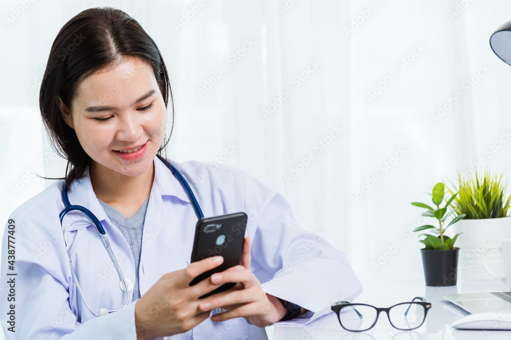 Asian doctor young beautiful woman smiling using working or holding with smart mobile phone and laptop computer at hospital desk office, technology healthcare medical concept Asian doctor young beautiful woman smiling using working or holding with smart mobile phone and laptop computer at hospital desk office, technology healthcare medical concept