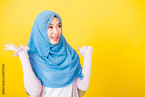 Asian Muslim Arab, Portrait of happy beautiful young woman Islam religious wear veil hijab funny smile she victories expression raises hands glad excited cheerful isolated yellow background © sorapop