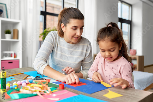 family, art and craft concept - mother spending time with her little daughter making applique of color paper at home