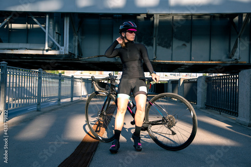 A view of a female cyclist in the morning, beautifully lit by the sun, resting after a workout. Morning training on a bike along the embankment. Sport equipment.