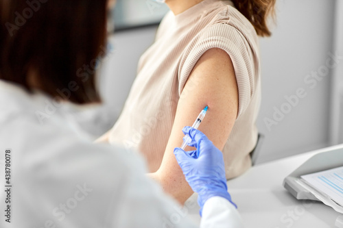 health  medicine and pandemic concept - close up of female doctor or nurse wearing protective medical gloves with syringe vaccinating patient at hospital