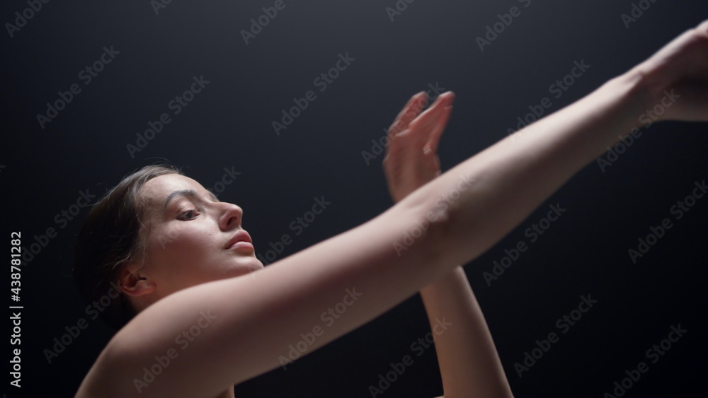 Fototapeta premium Ballet dancer practicing in dark background. Ballerina moving hands indoors.