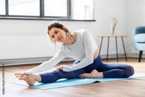 fitness, sport and healthy lifestyle concept - young woman doing yoga exercises on mat at home