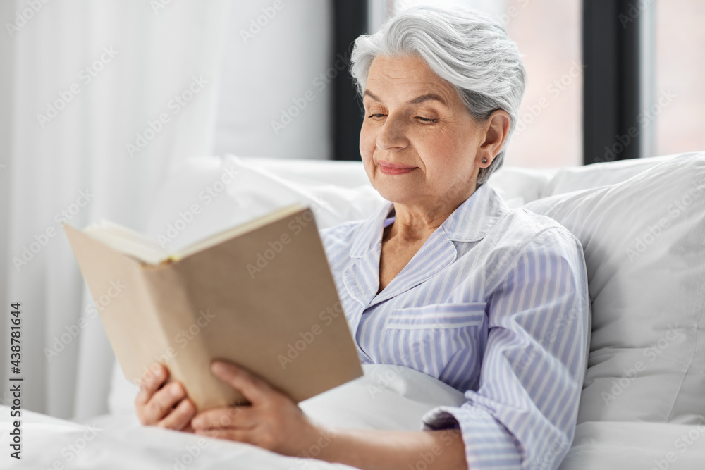 technology, old age and people concept - senior woman reading book in bed at home bedroom