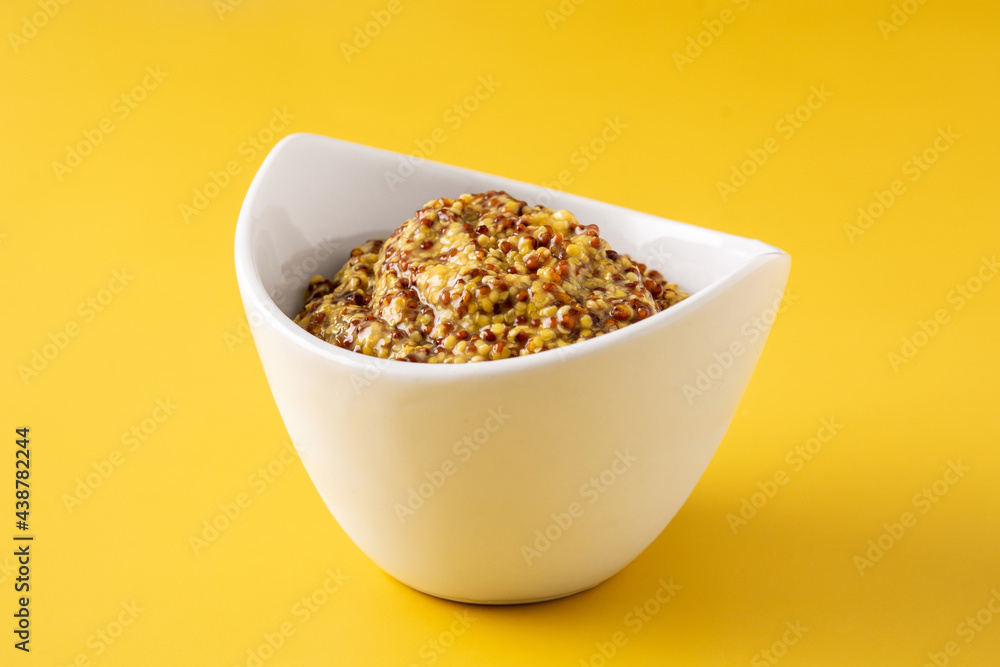 Mustard sauce in white bowl on yellow background Mustard sauce in white bowl on yellow background