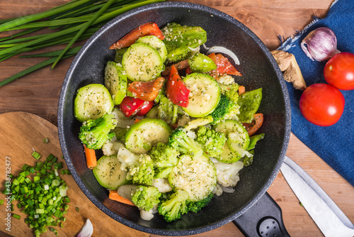 Vegetarian dish of broccoli, zucchini, onions and tomato in a skillet. Vegetables are stewed in a wok. Frying pan with vegetables on the table, top view