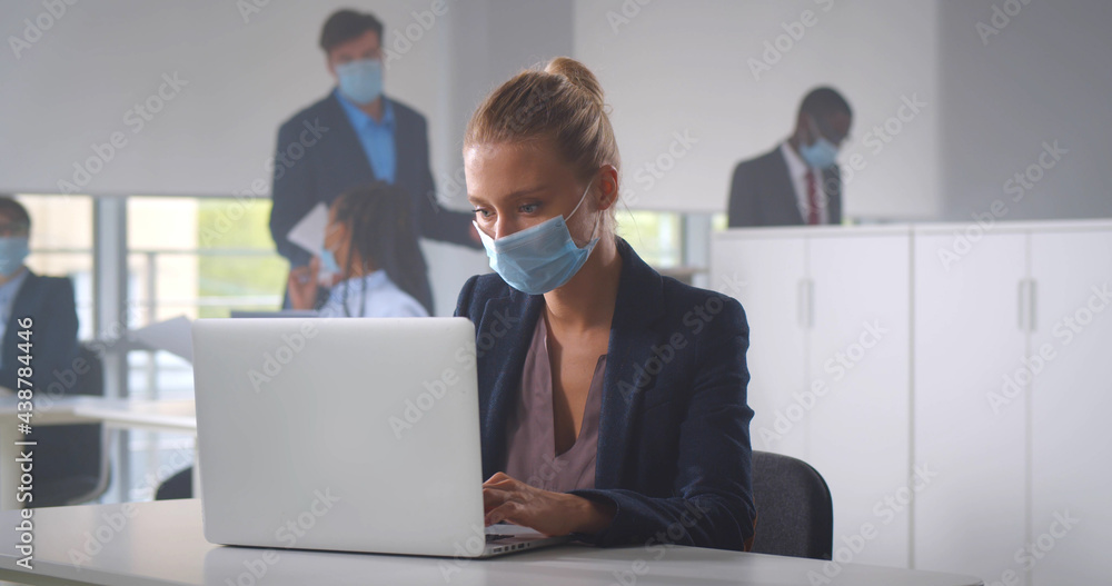 Businesswoman sitting in office in front of computer wearing face mask Businesswoman sitting in office in front of computer wearing face mask