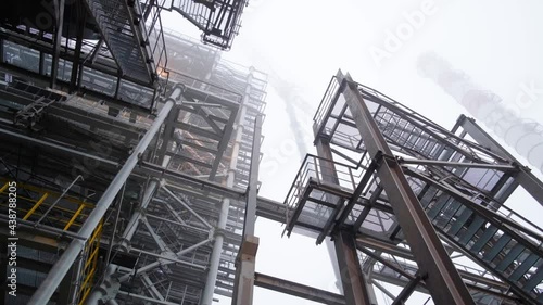 Movement under metal structures. Epic industrial landscape. Chimney obscured by fog in the background.