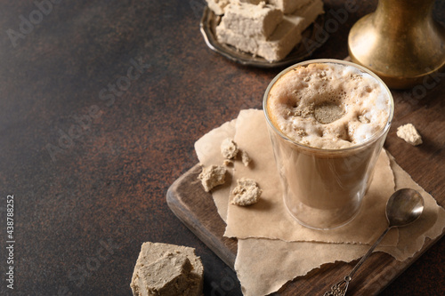 Tasty homemade coffee latte with halva in glass cup on dark brown background. Close up. Copy space.