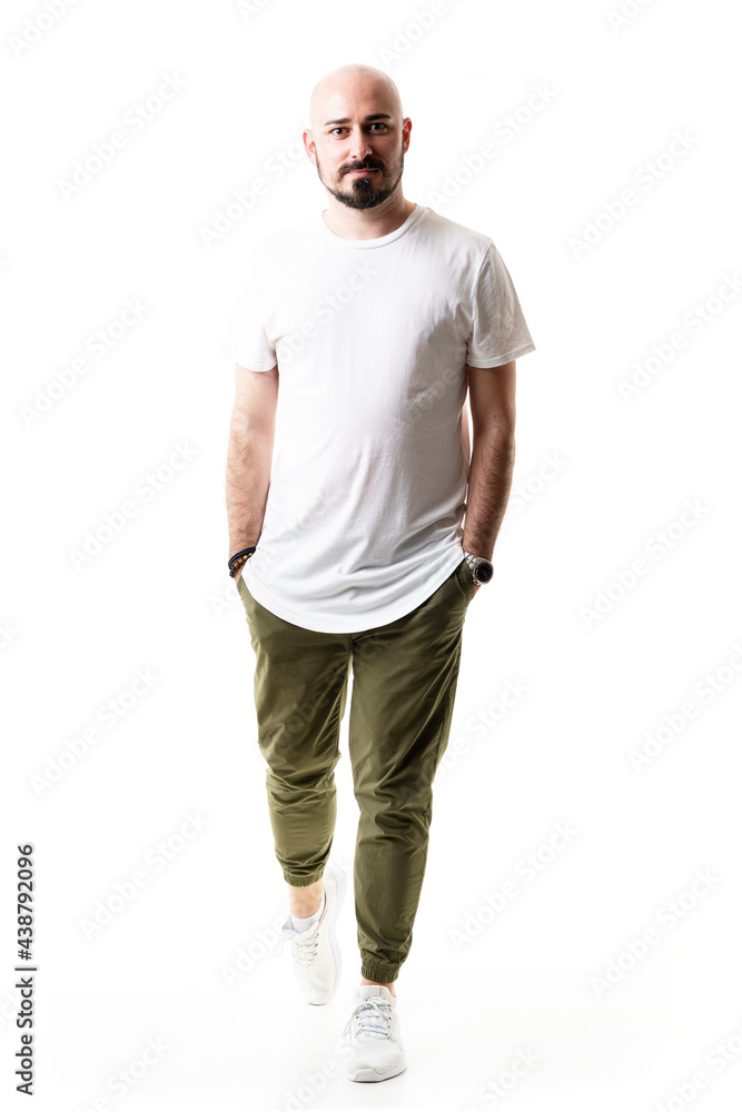 Cool modern confident bald bearded man walking with hands in pockets. Full body length isolated on white background