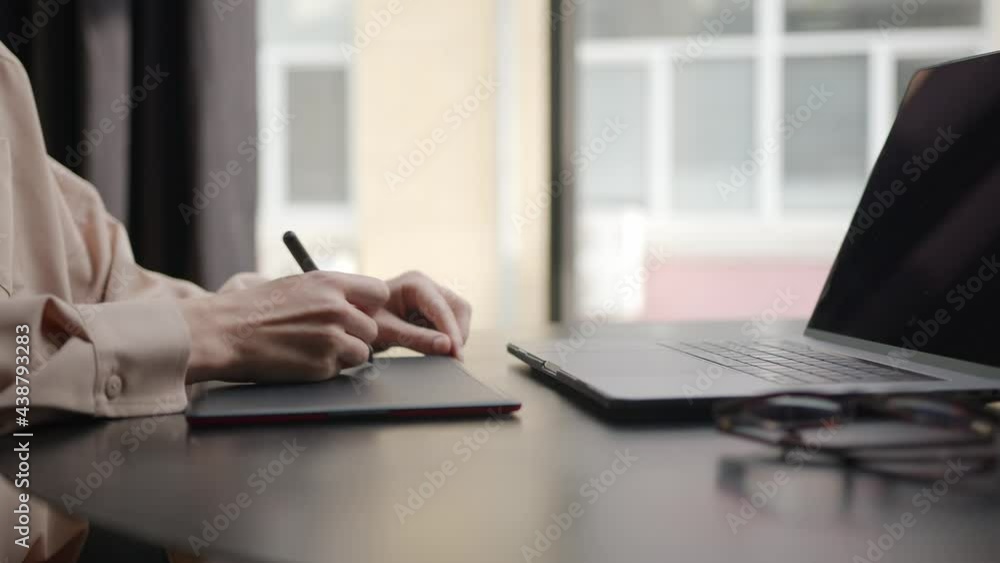 Closeup of woman holding a digital pen, drawing fast using a graphic tablet and laptop in light office room. Portable devices for artists. Concept of project and freelancer Closeup of woman holding a digital pen, drawing fast using a graphic tablet and laptop in light office room. Portable devices for artists. Concept of project and freelancer