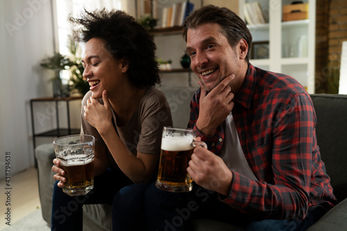 Boyfriend and girlfriend drinking beer at home. Happy couple watching sports game on tv..