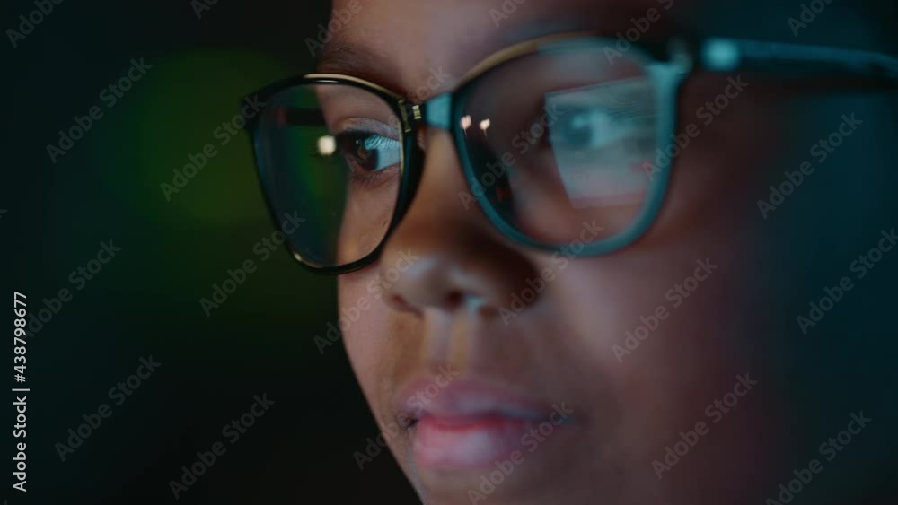 Close Up Portrait of a Cute Young Teenage Multiethnic Black Girl in a Dark Cozy Room at Home. Young Female Wears Glasses that Reflect School Homework from Her Laptop Computer Screen in Them. Close Up Portrait of a Cute Young Teenage Multiethnic Black Girl in a Dark Cozy Room at Home. Young Female Wears Glasses that Reflect School Homework from Her Laptop Computer Screen in Them.