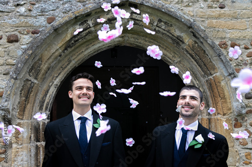 Smiling gay grooms leave church after getting married with confetti falling around them. photo