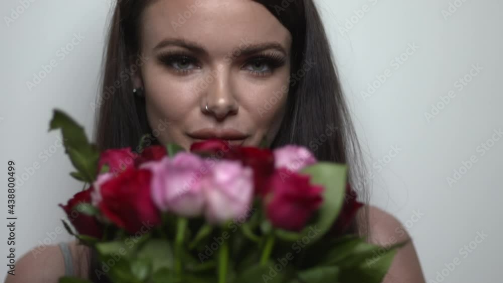 Pretty model holding a bouquet of red and pink roses. Girl on white background. Attractive female smelling a bouquet of roses while looking at the camera. Woman with flowers. Pretty model holding a bouquet of red and pink roses. Girl on white background. Attractive female smelling a bouquet of roses while looking at the camera. Woman with flowers.