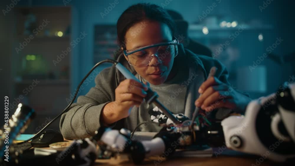 Young Teenage Multiethnic Schoolgirl is Studying Electronics and Soldering Wires and Circuit Boards in Her Science Hobby Robotics Project. Girl is Working on a Robot in Her Room. Education Concept. Young Teenage Multiethnic Schoolgirl is Studying Electronics and Soldering Wires and Circuit Boards in Her Science Hobby Robotics Project. Girl is Working on a Robot in Her Room. Education Concept.