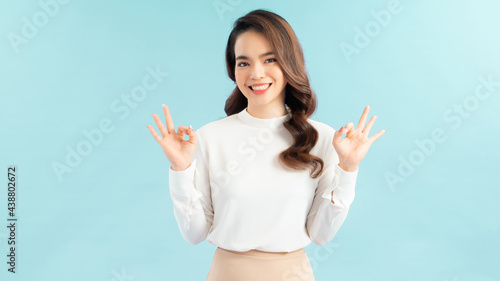 Young happy woman in white t-shirt, winking and showing okay signs, smiling pleased, recommend advertisement, approve product over blue background