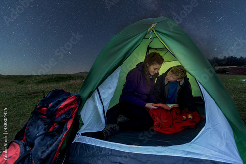 Woman and boy in a tent at night reading a book