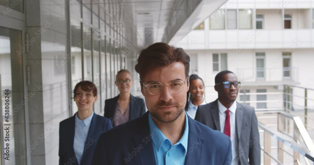 Successful team of diverse business people confidently striding along office building
