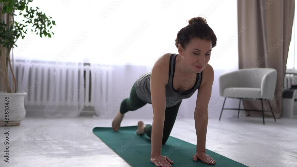 Beautiful brunette is working out at home on a yoga mat. The girl performs exercises for the muscles of the legs and back. Home workout fitness activity Beautiful brunette is working out at home on a yoga mat. The girl performs exercises for the muscles of the legs and back. Home workout fitness activity