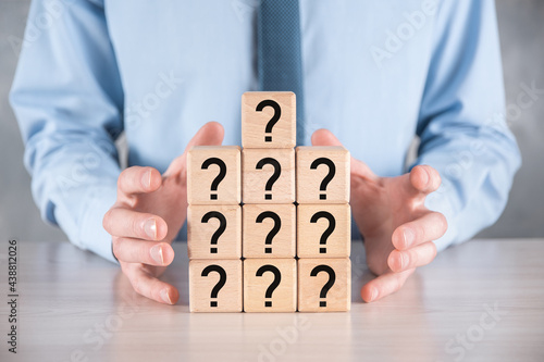 Businessman hold and put wooden cube block shape with question marks on grey table. Space for text.concept for confusion, question or solution