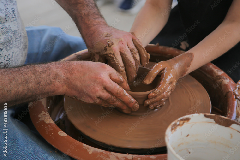  Male's and child's hands  makes a pot on the pottery wheel. Close view the potter's hands make a vase out of fine clay. Creativity․ The idea of ​​traditional crafts.  Handmade pots. 