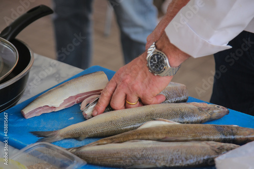 Man's hand clean fish on board. Man with a wedding ring and clock preparing food in kitchen.