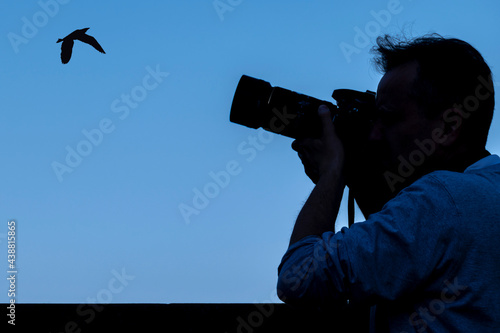 Silhouette of a photographer who is photographing a bird against the blue sky