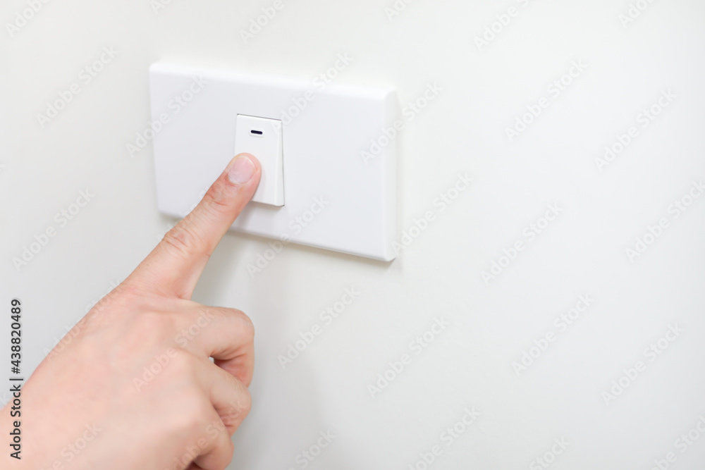 Close up of a business man finger is turning on or off on light switch in office white wall with Copy space, Save energy and environment for earth day background concept Close up of a business man finger is turning on or off on light switch in office white wall with Copy space, Save energy and environment for earth day background concept