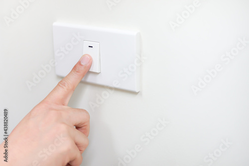 Close up of a business man finger is turning on or off on light switch in office white wall with Copy space, Save energy and environment for earth day background concept