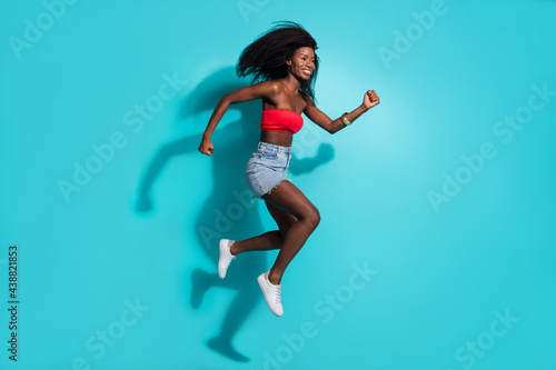 Fototapeta Naklejka Na Ścianę i Meble -  Full body photo of brunette afro american young woman jump up run empty space isolated on blue color background