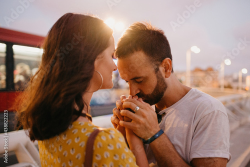 A close photo of a man who is kissing the hands of his girlfriend on a white bridge in Valencia. A couple of tourists on a date in the warm evening.