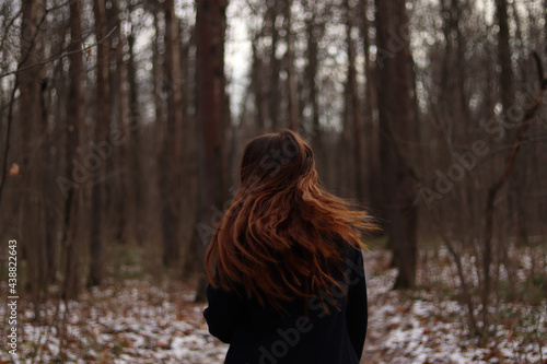 Young woman in autumn forest waving her long hair, dark coat, look from behind, girl in the woods, view on her back