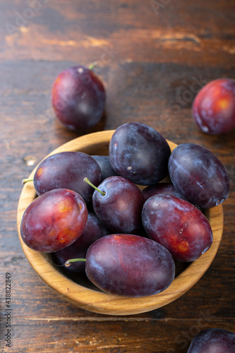 Fresh plums in a wooden bowl on a brown table.