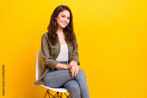 Portrait of attractive confident cheerful girl sitting on chair isolated over vibrant yellow color background