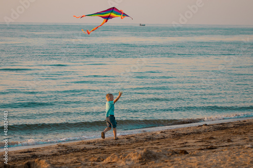 Obraz na płótnie child flies a kite on the beach. A boy runs along the seashore with a bright kite w salonie