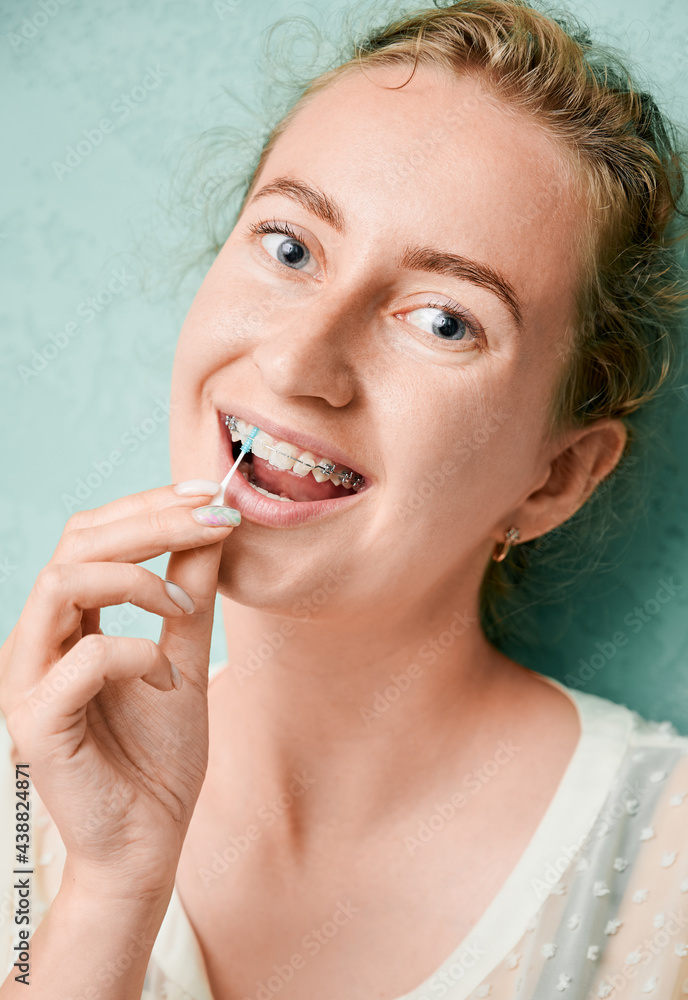 Portrait of a beautiful woman standing at the wall, demonstrating interdental brushing, wearing dental ceramic and metal brackets. Vertical closeup snapshot. Cleaning teeth Portrait of a beautiful woman standing at the wall, demonstrating interdental brushing, wearing dental ceramic and metal brackets. Vertical closeup snapshot. Cleaning teeth