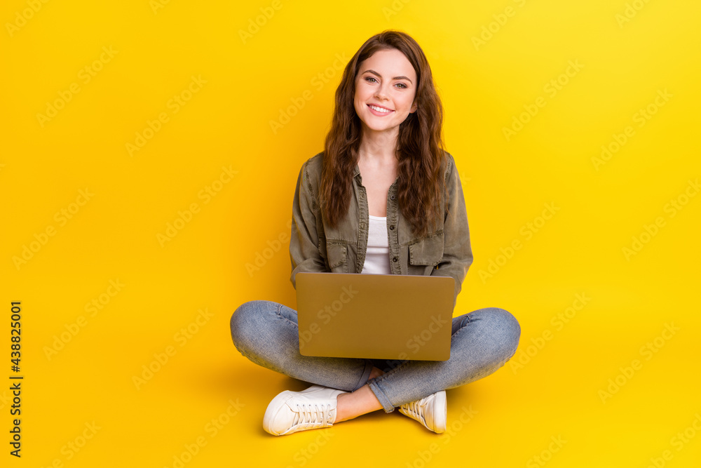Naklejka premium Photo of nice pretty young woman dressed brown shirt sitting floor typing laptop isolated yellow color background