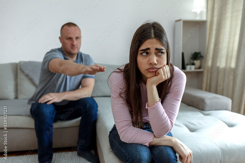 Cropped shot of a couple having a disagreement at home. Young couple in quarrel at home. Sad young Caucasian woman sitting on sofa with boyfriends. Frustrated young couple having marriage problems. Cropped shot of a couple having a disagreement at home. Young couple in quarrel at home. Sad young Caucasian woman sitting on sofa with boyfriends. Frustrated young couple having marriage problems.
