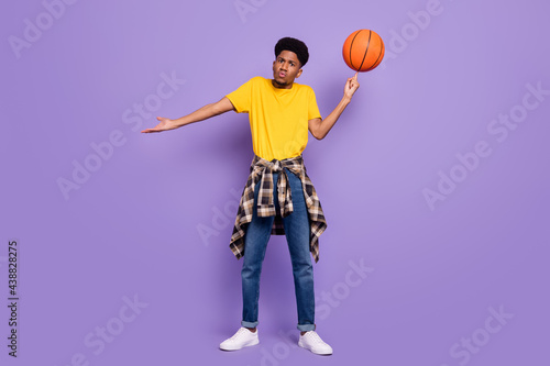 Full size photo of unhappy afro american young clueless man hold ball spin isolated on violet color background