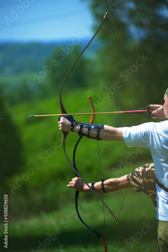 professional archer shooting with modern longbow at forest 