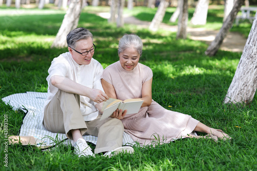 Happy old couple sitting on the park grass reading