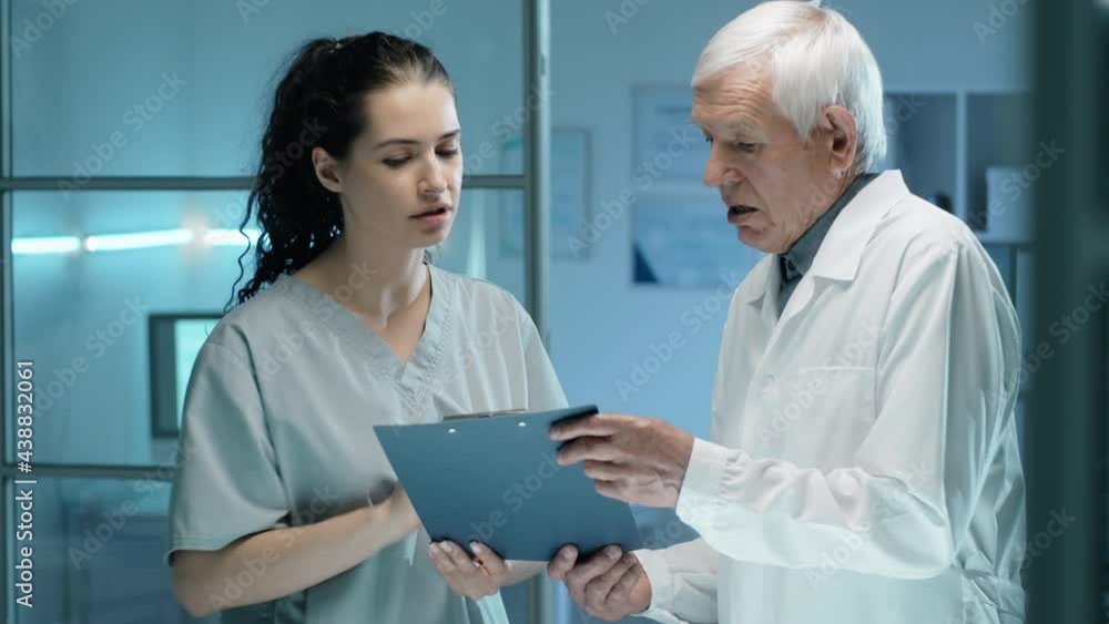 Young female lab technician discussing paper on clipboard with senior male scientist during workday Young female lab technician discussing paper on clipboard with senior male scientist during workday